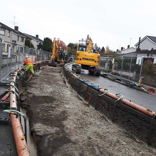 Workmen and digger laying pipeline in road